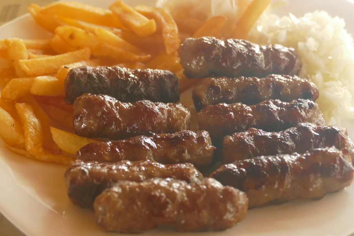 A plate of grilled ćevapi with fries and chopped onion